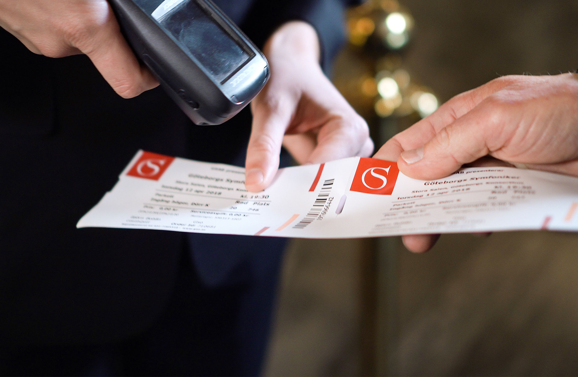 Hand som sträcker fram sin biljett mot en publikvärd.