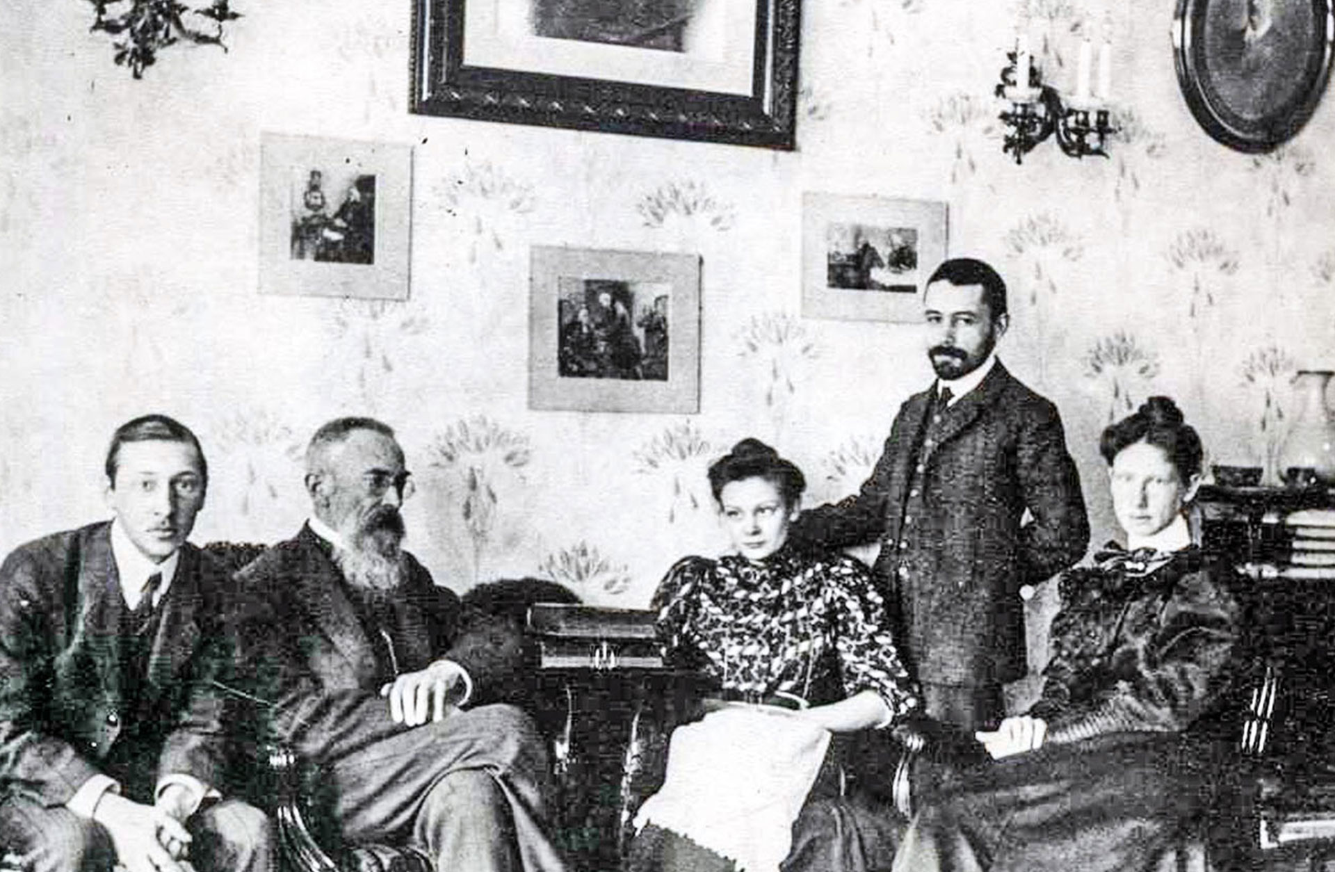 Igor Stravinsky och Nikolaj Rimskij-Korsakov med familjemedlemmar och vänner. De sitter i en soffa och tittar in i kameran.