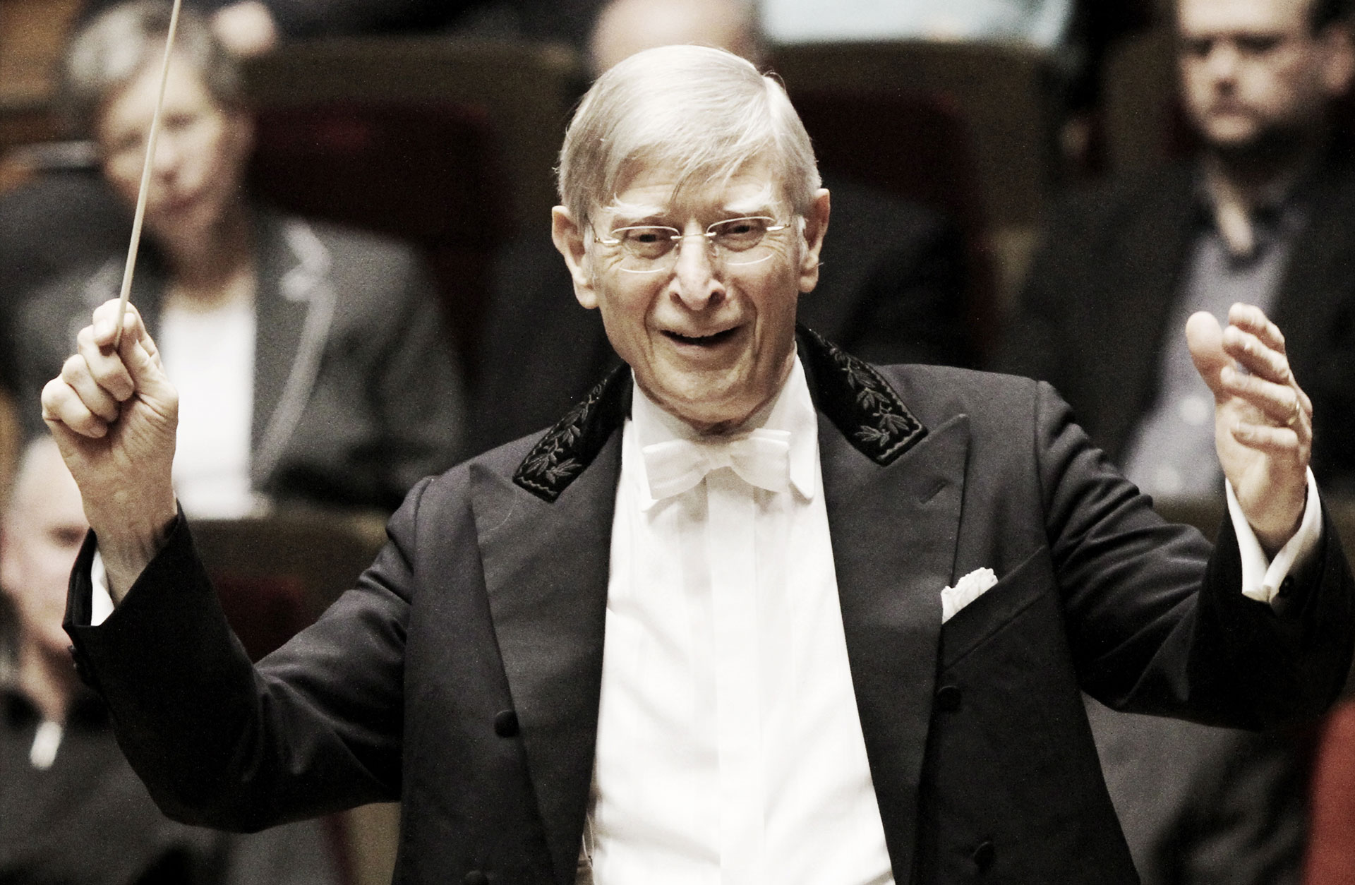 Dirigenten Herbert Blonstedt i en glad gest med taktpinnen i handen, orkestermusikerna syns bakom honom.