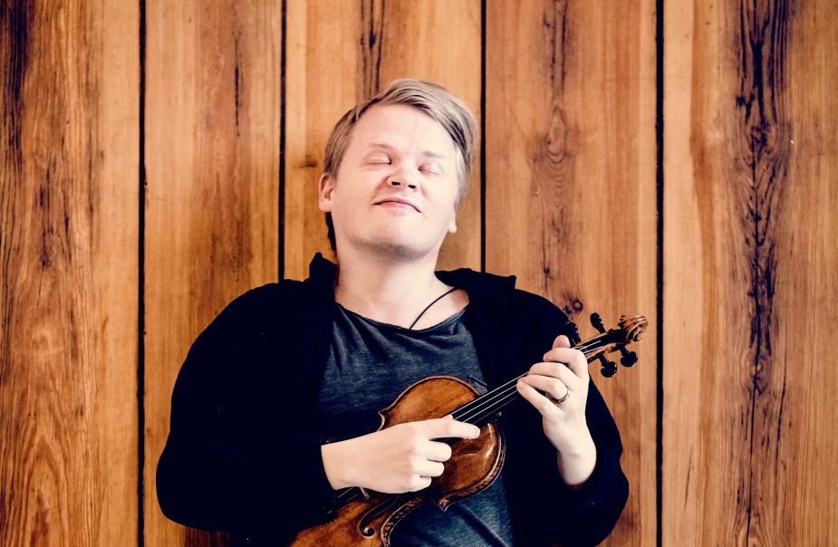 Violinisten Pekka Kuusisto blundar, lutar sig mot en vägg och knäpper på violinen med fingrarna.