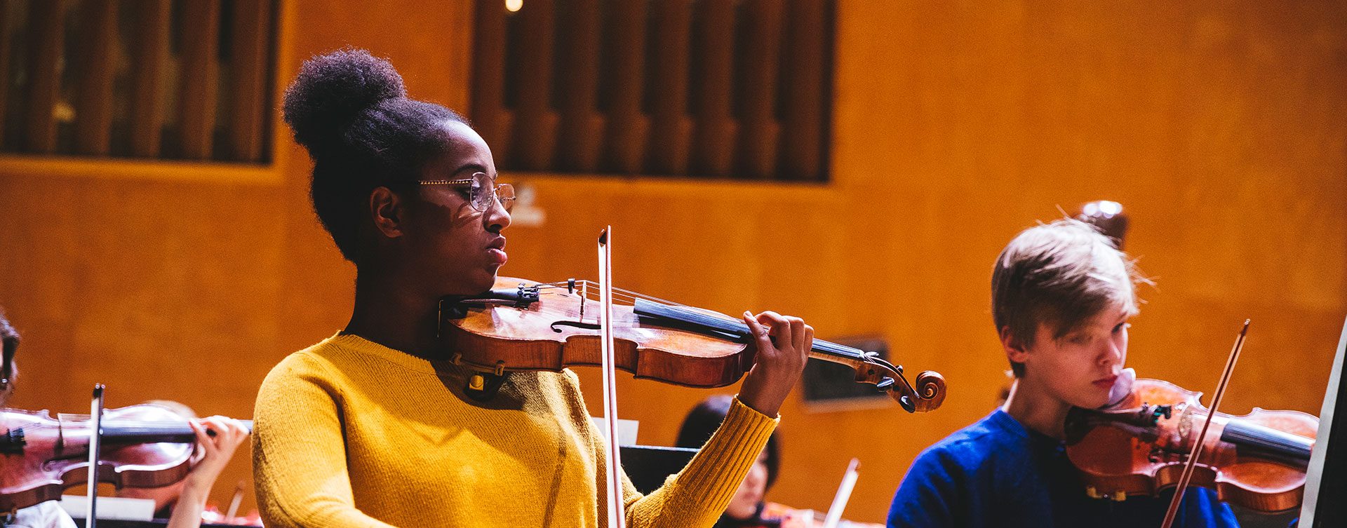 Ung musiker spelar violin, flera unga musiker syns bakom och vid sidan av henne.