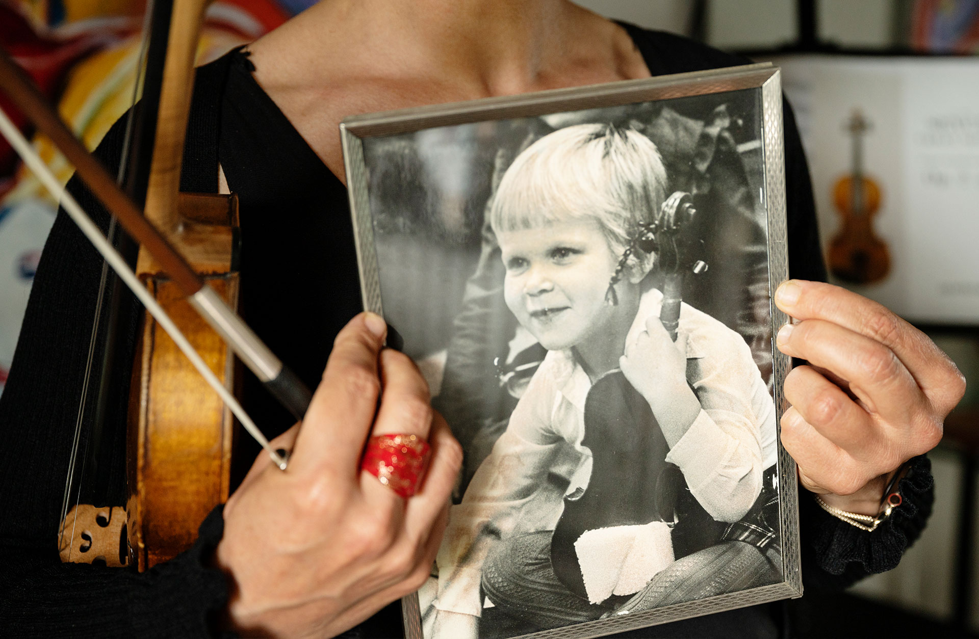 Elin håller i ett inramat svartvitt porträtt föreställande Elin som liten med en fiol i famnen.