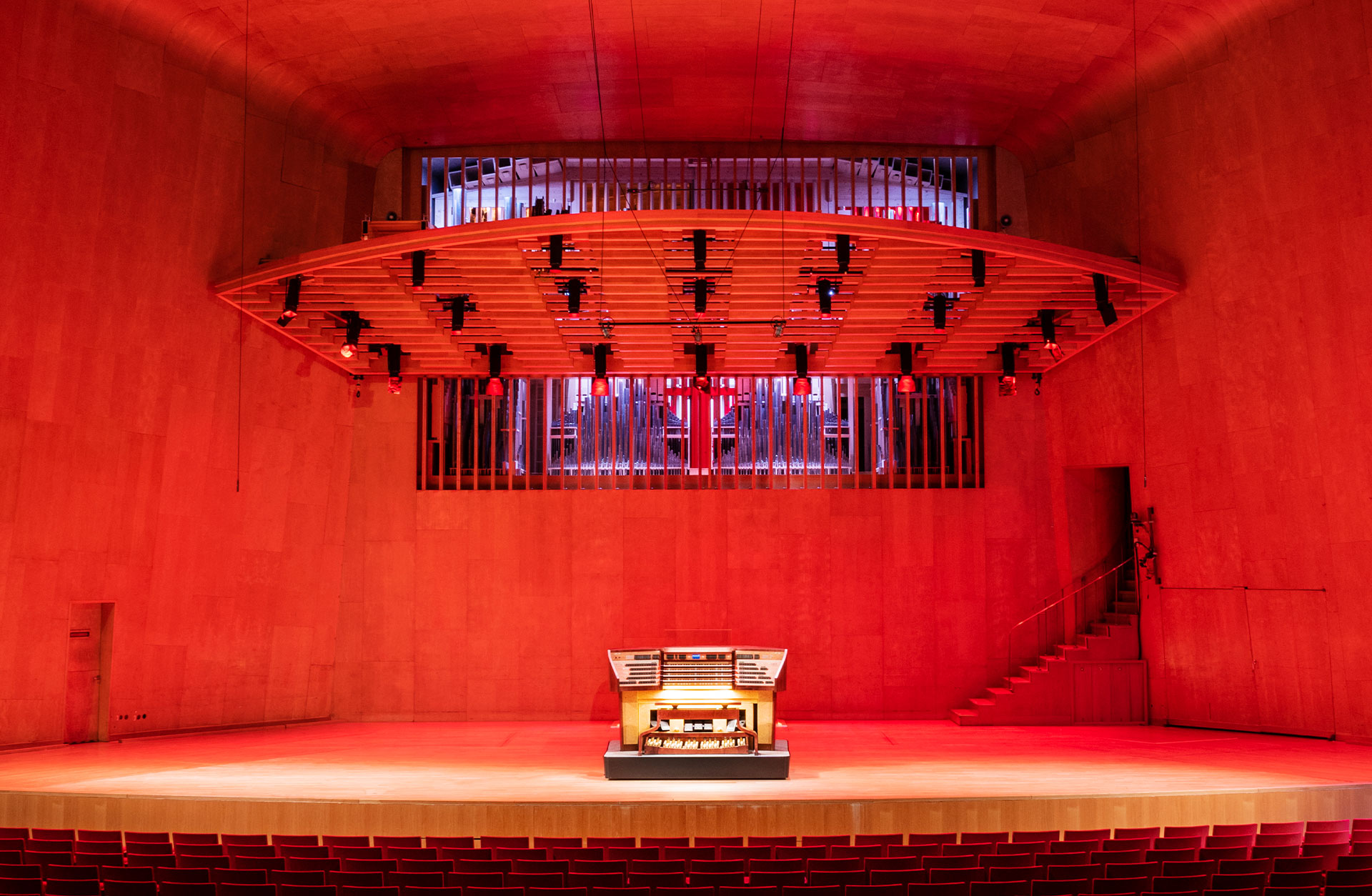 Orgelns spelbord står på podiet. Ett rött ljus fyller scenen.