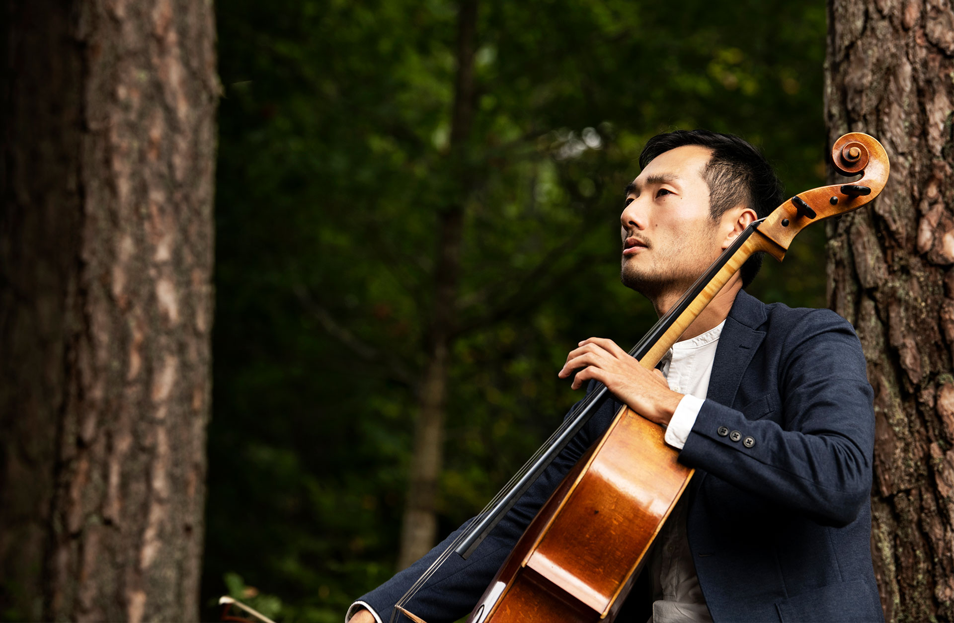 Jun Sasaki sitter utomhus i skogen och spelar på sin cello.