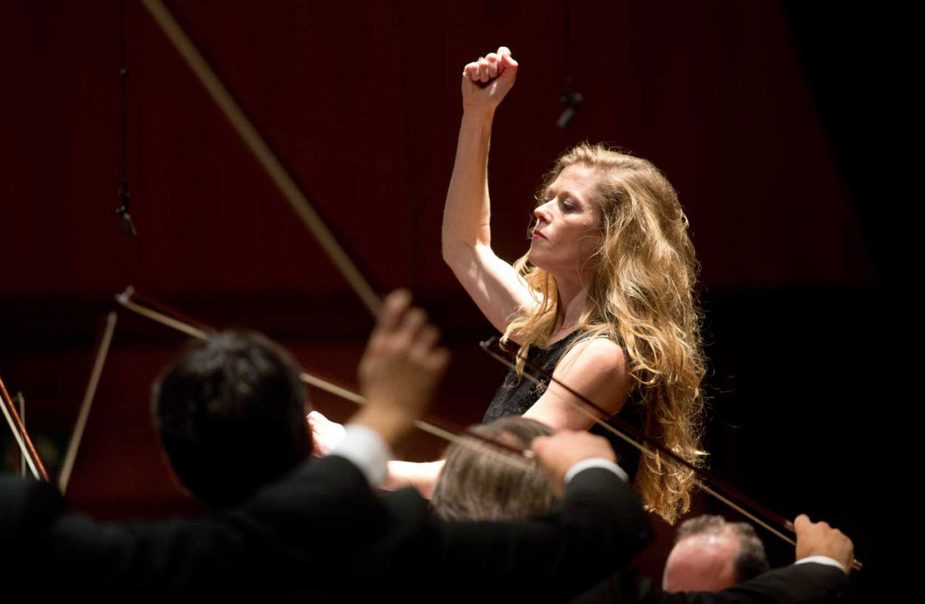Kvinna med långt hår dirigerar med orkester