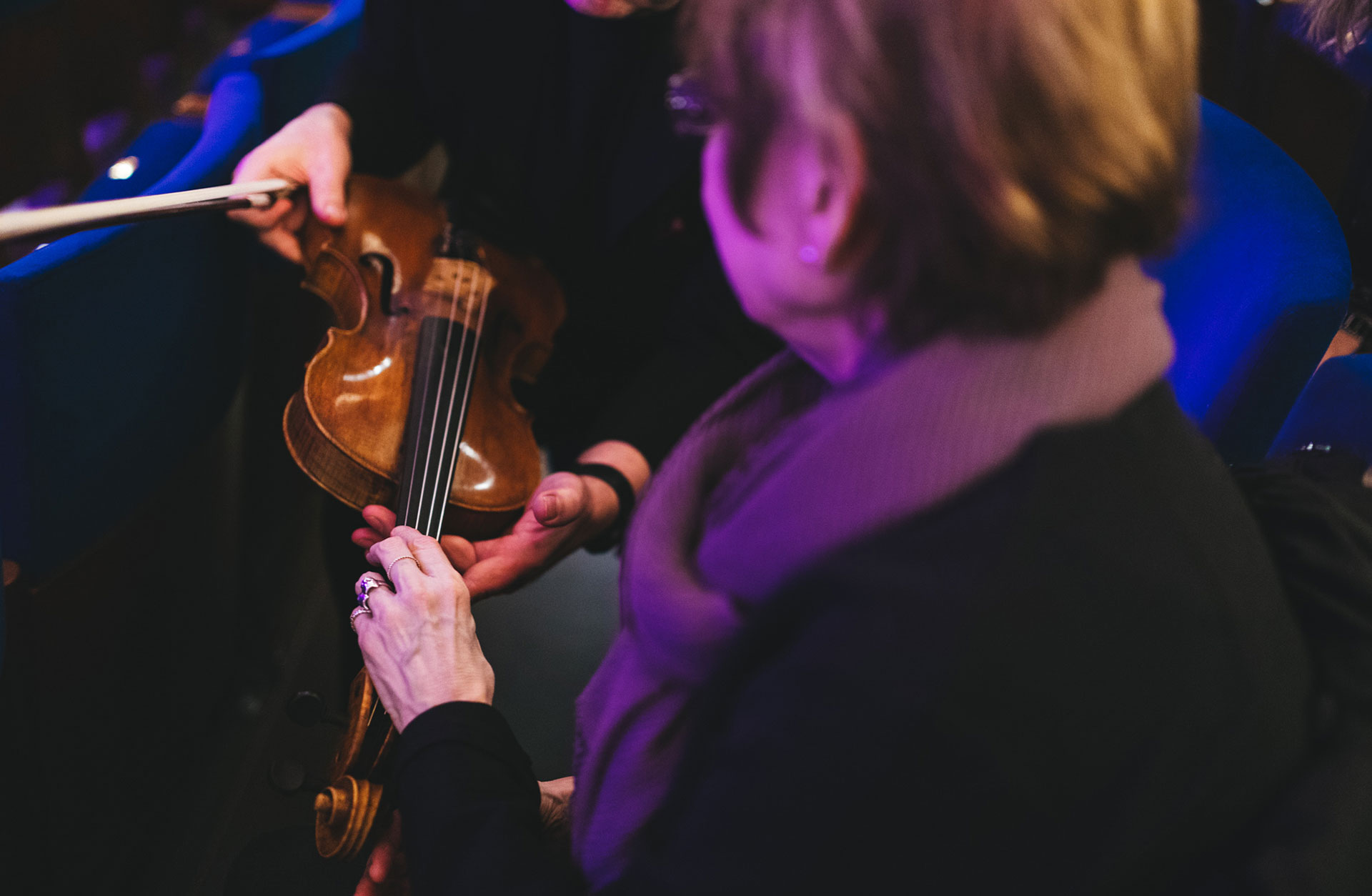 En violinist håller fram sin fiol så att en i publiken kan känna på den.