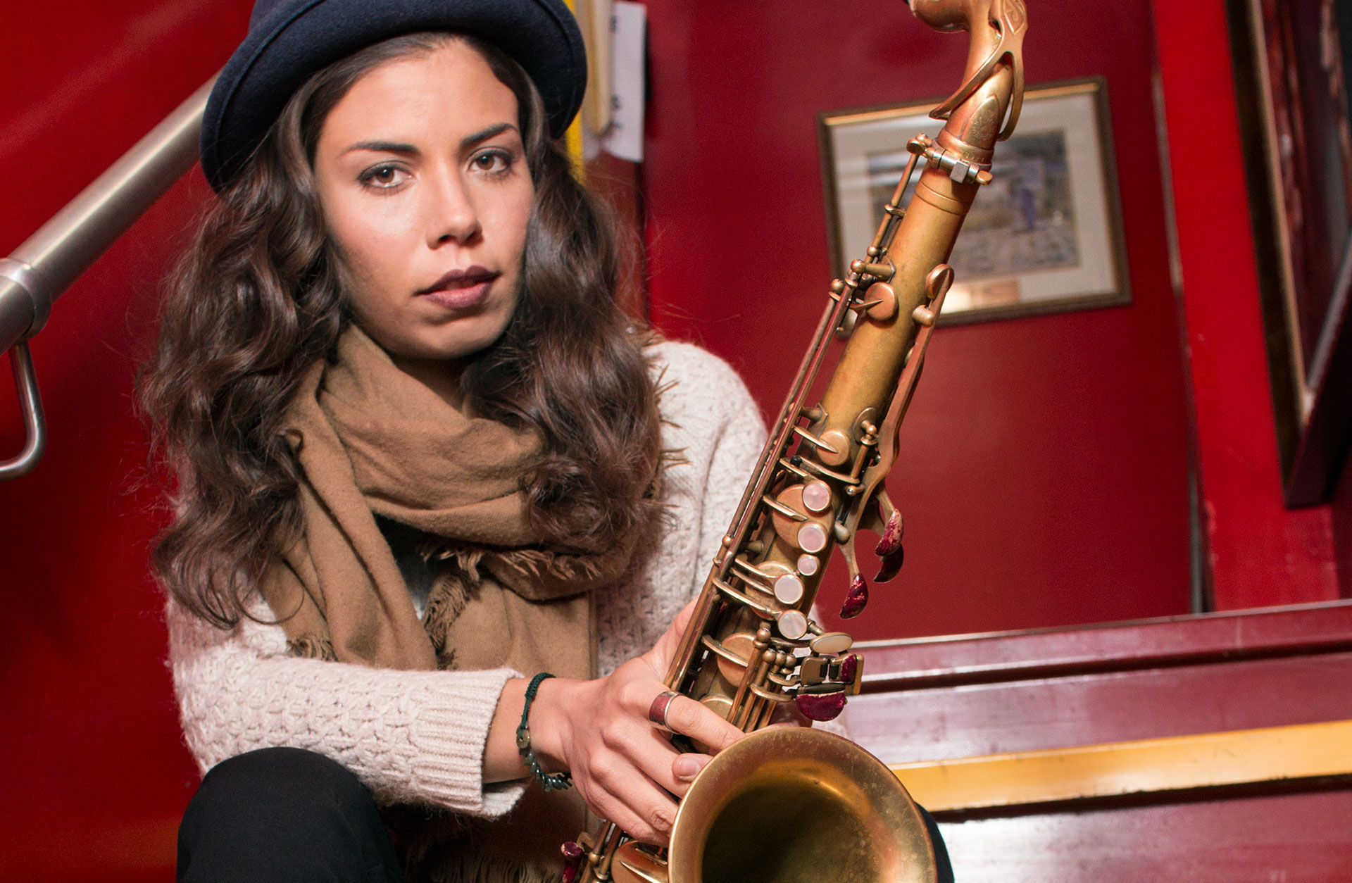 Melissa Aldana sitter på en trappa med sin saxofon i händerna.
