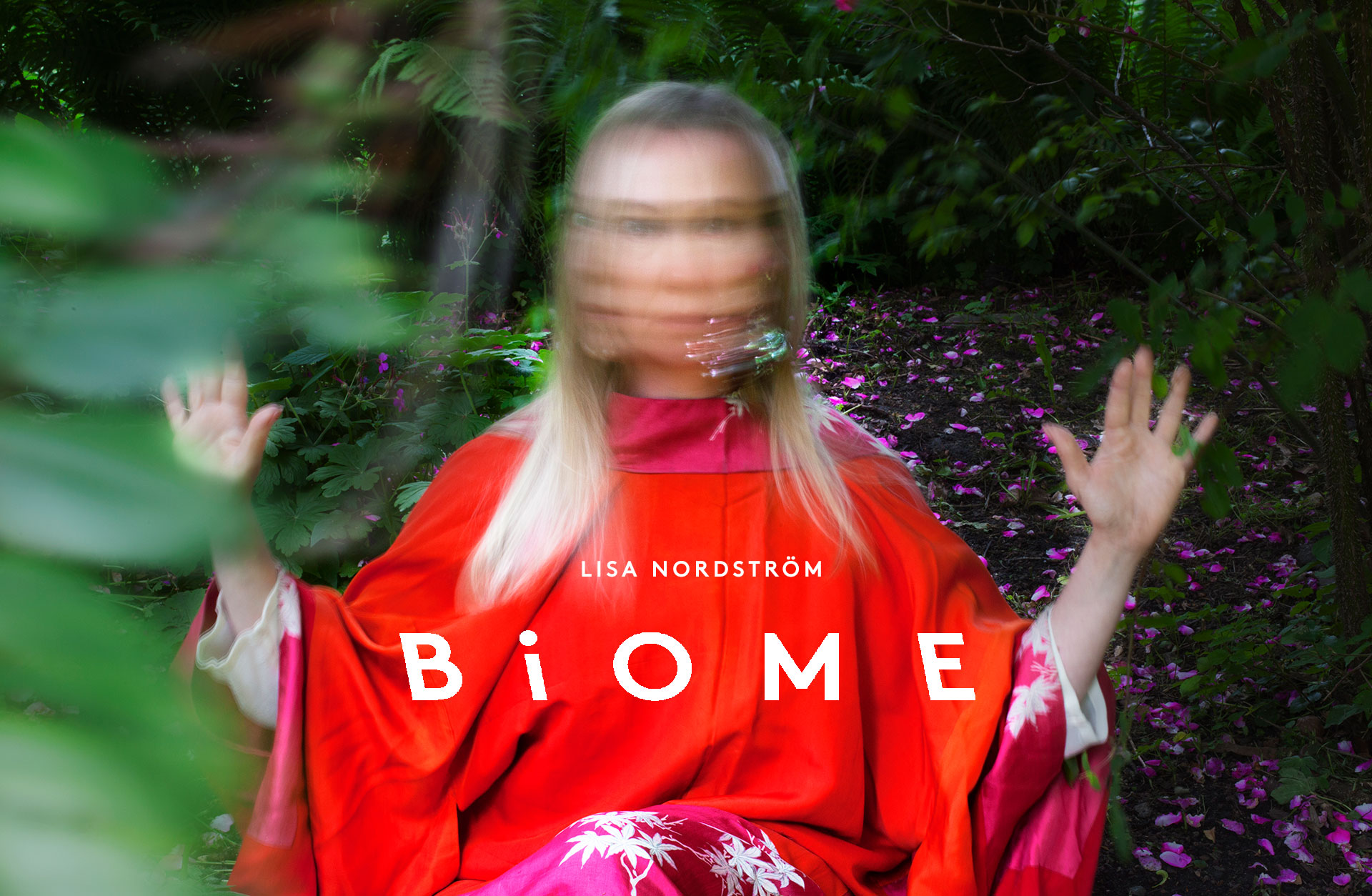 Lisa Nordström, klädd i rött, sitter i en skog. Hennes ansikte är suddigt och hon håller upp sina handflator.