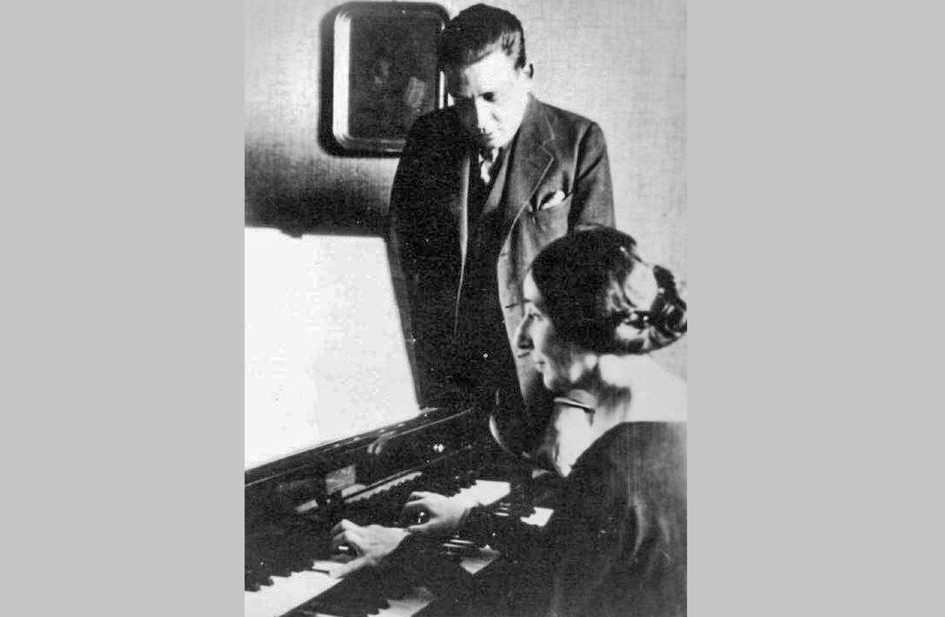 Svartvit bild där Francis Poulenc medstår vid sidan av pianisten Wanda Landowska när hon spelar piano.