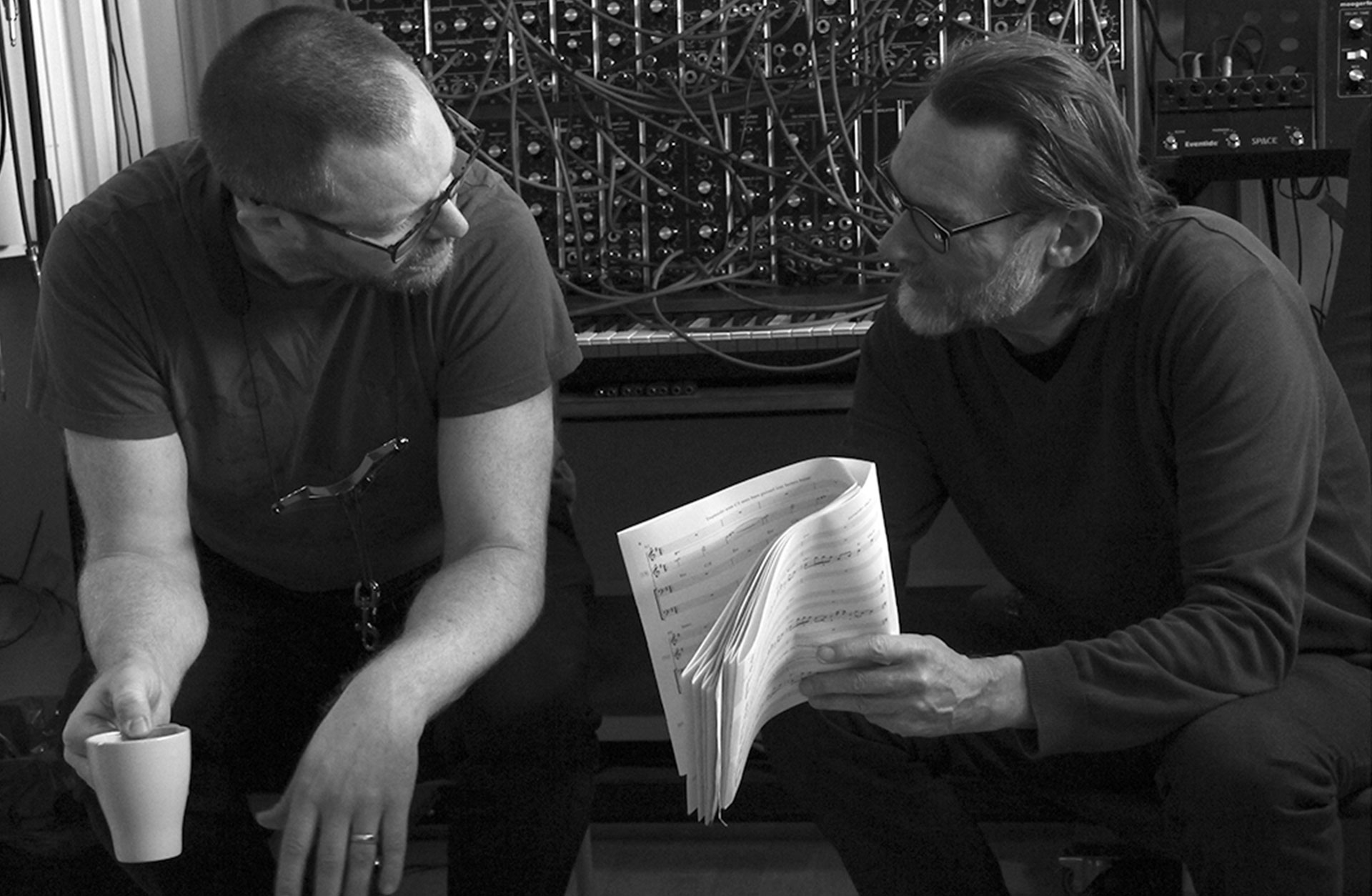 Björn Cedergren och Kjell Jansson diskuterar noter i en musikstudio.