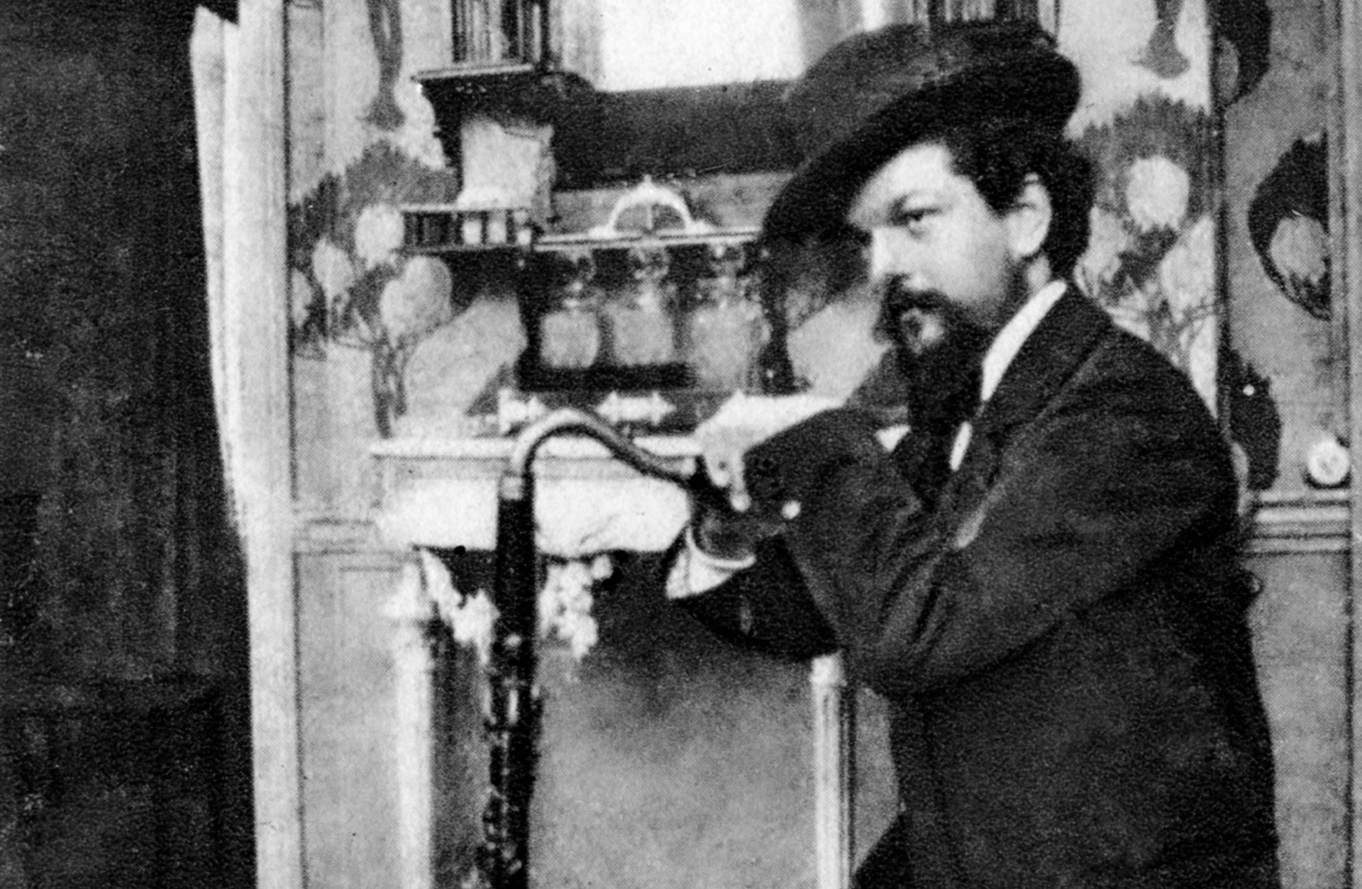 En ung Claude Debussy iklädd kostym och hatt. Han håller i en fagott.