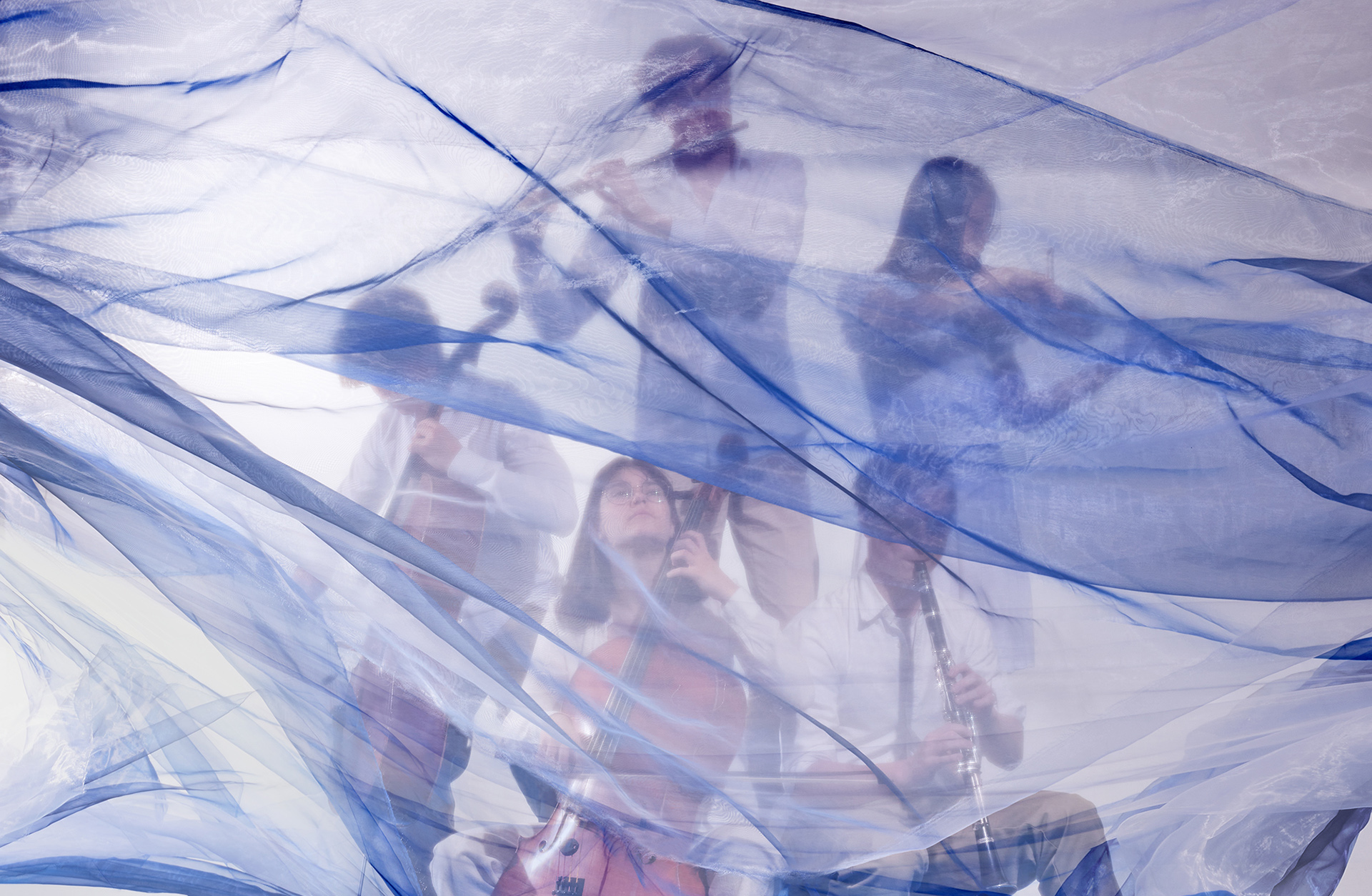 fem unga musiker som spelar sina instrument framför ett blått tyg som fladdrar i  vinden