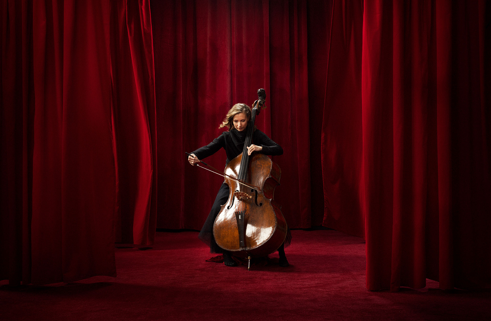 Kontrabasisten Jenny Rydeberg spelar på sitt instrument i ett rött sammetsrum