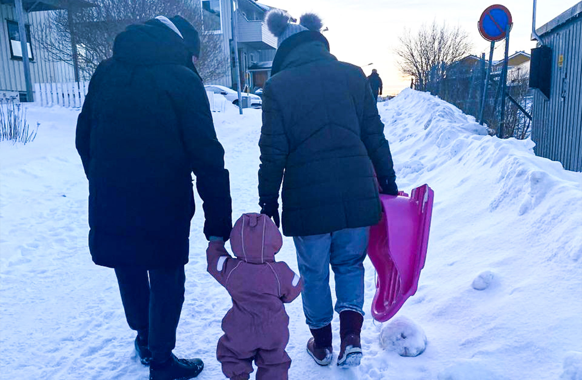 Man ser Igor med familj bakifrån. De går i snön. Igår håller sitt barn i handen och hans fru bär på en rosa pulka.