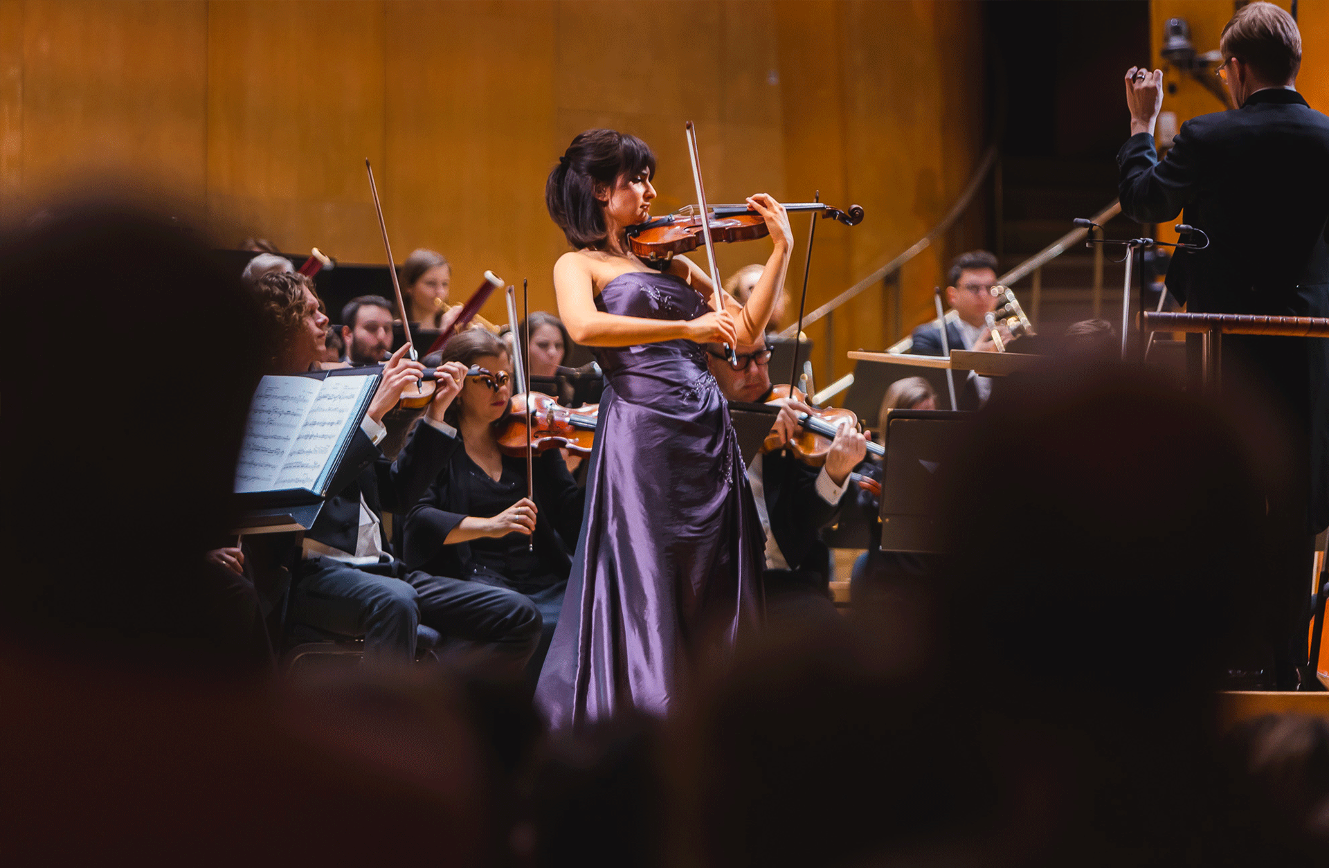 Violinist i lila klänning spelar inlevelsefullt framför orkestern.