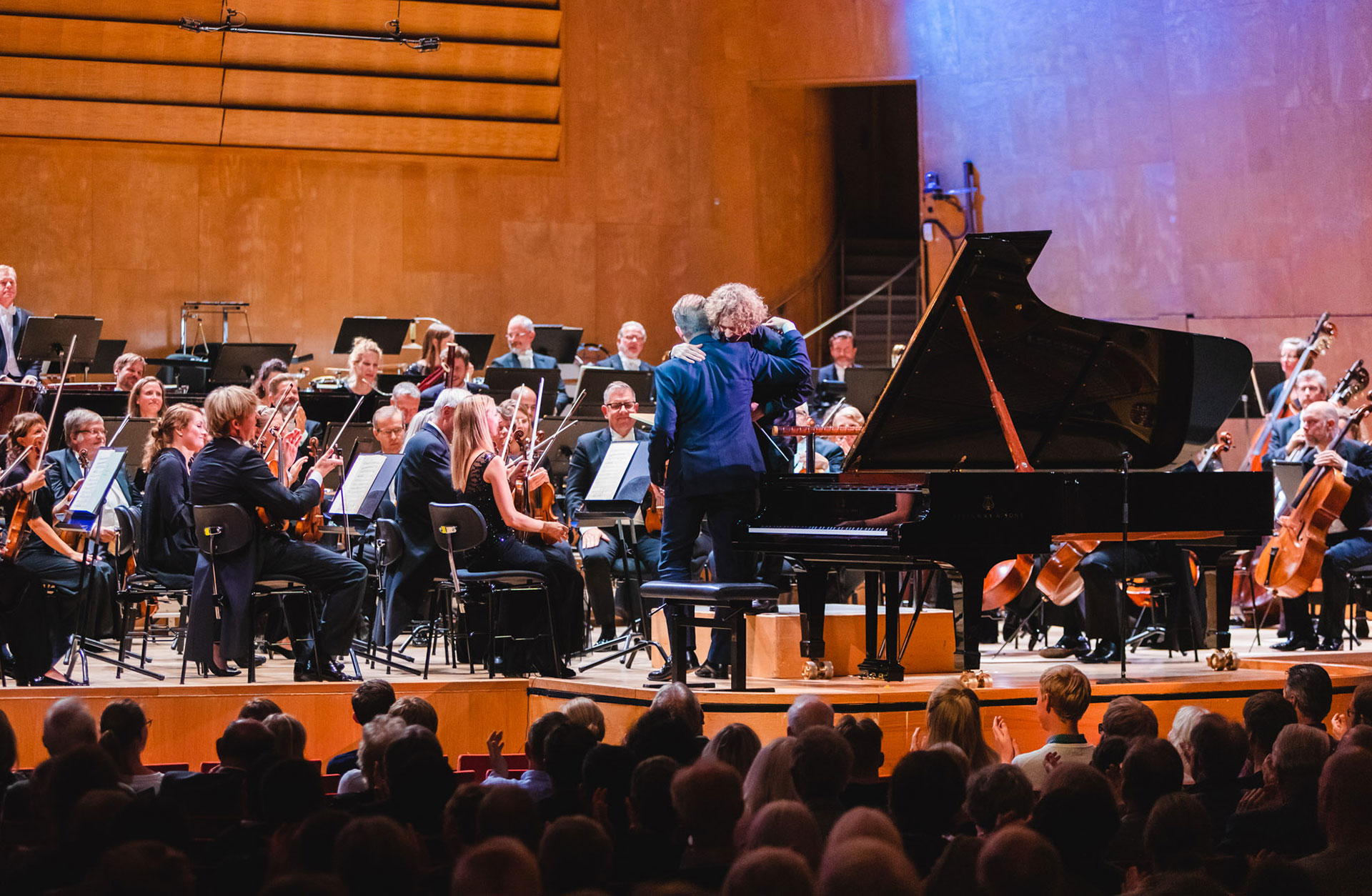Pianist och dirigent kramas på scenen efter konsertens slut, orkestern syns i bakgrunden.