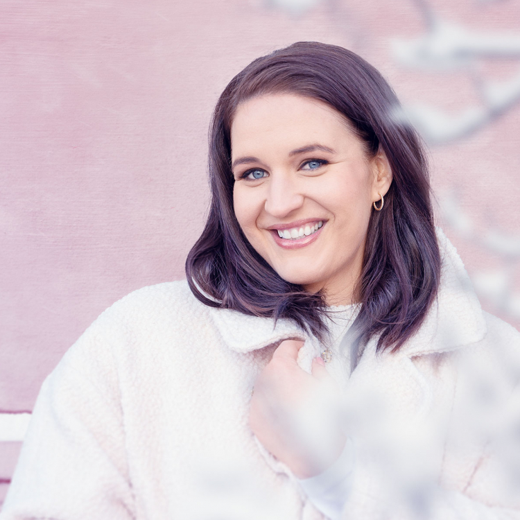 Sångerskan Lise Davidsen i vita vinterkläder mot rosa vägg.