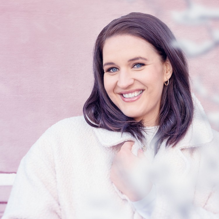 Sångerskan Lise Davidsen i vita vinterkläder mot rosa vägg.