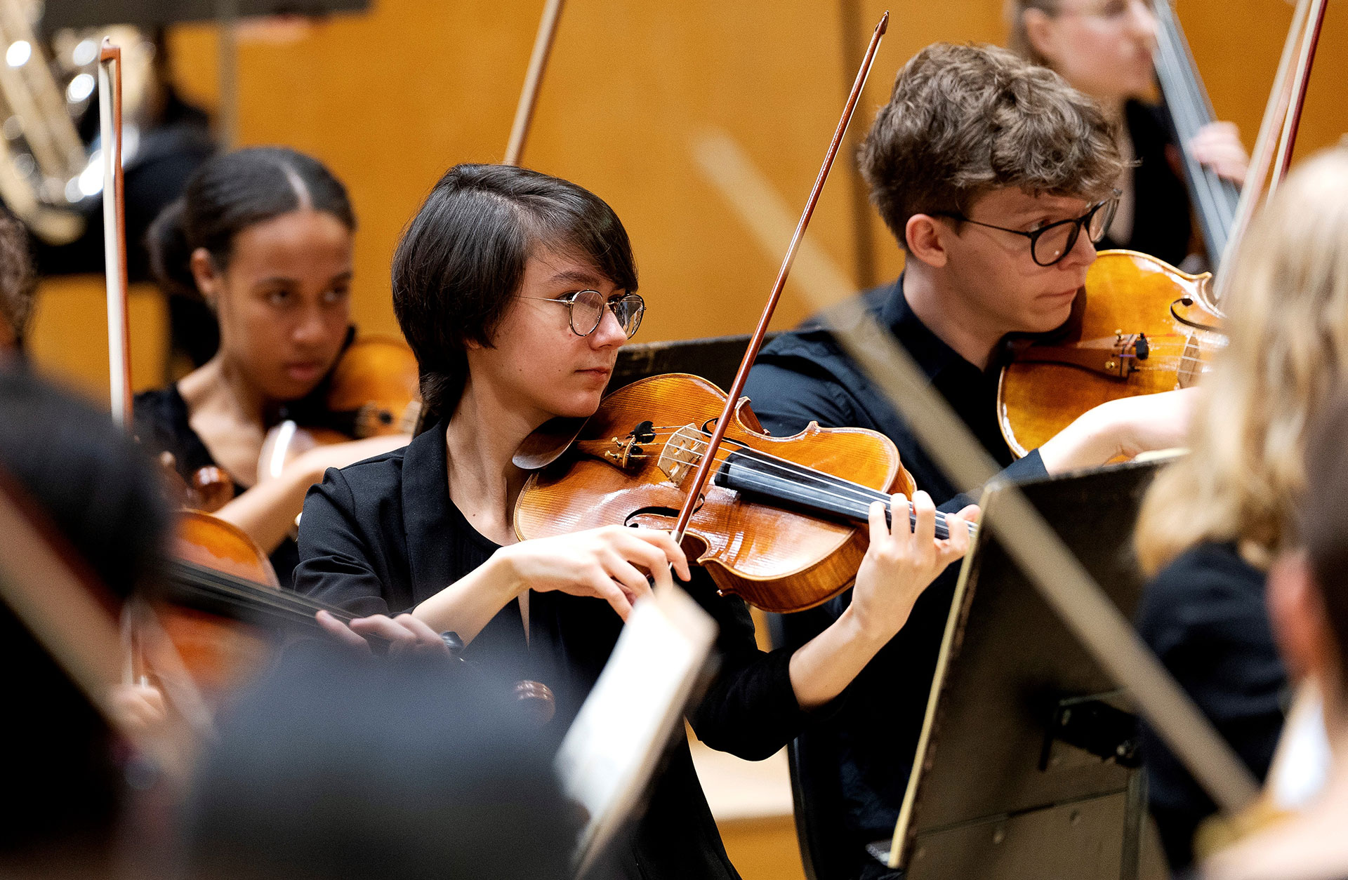 En ung kvinna i mörkt kortklippt hår spelar viola i en orkester.
