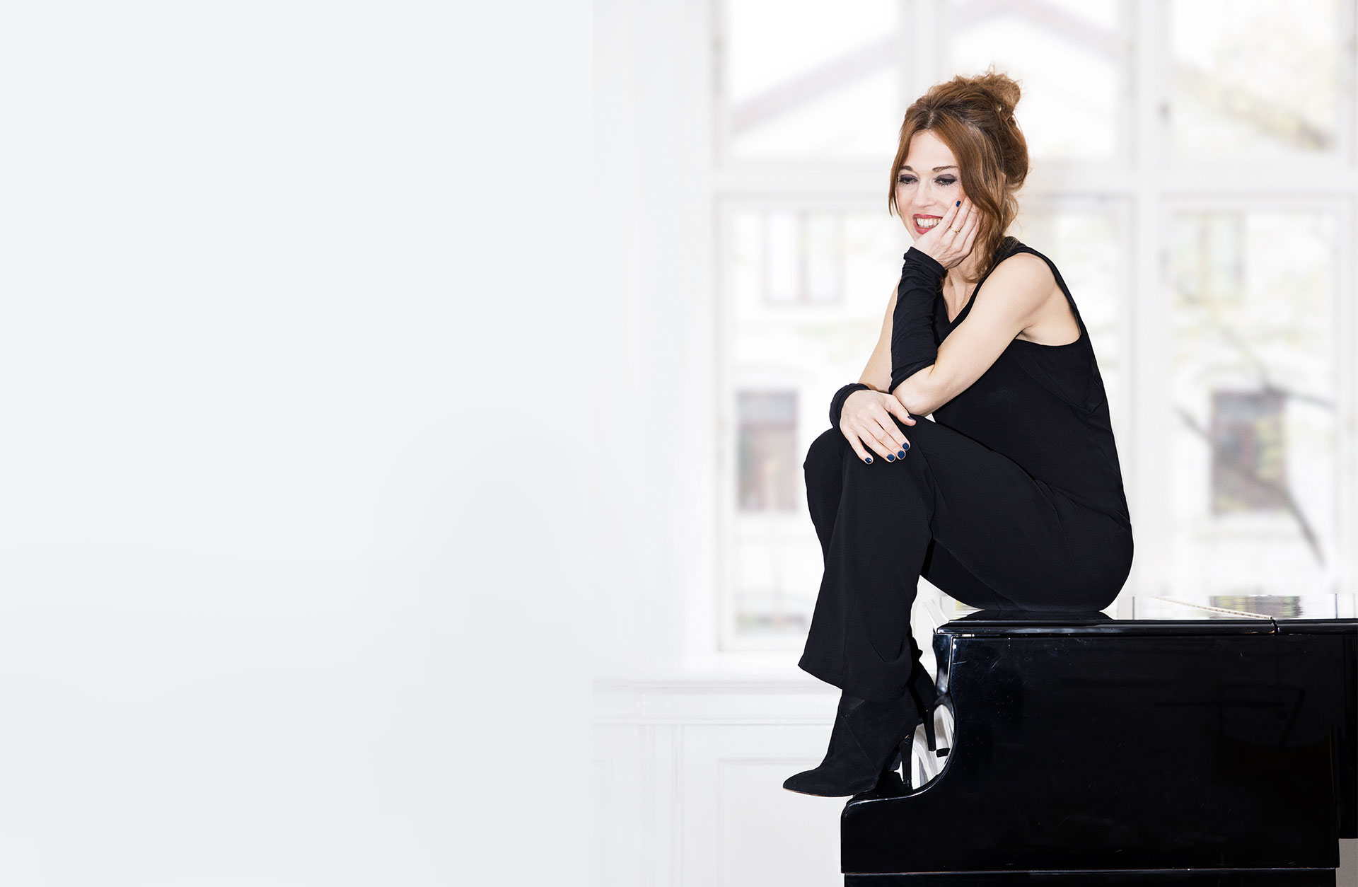 Kvinna sitter i profil på flygel. Svartklädd mot ljus bakgrund.