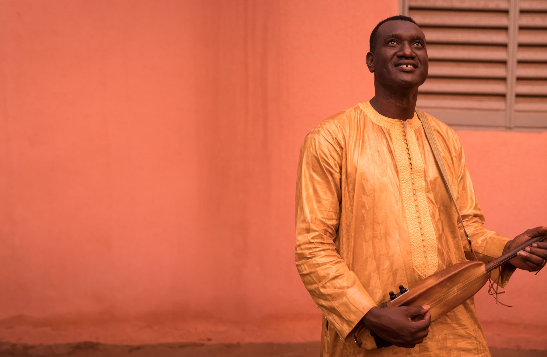 Bassekou Louyate är klädd i en fin gul tunika utomhus och spelar på sitt stränginstrument.