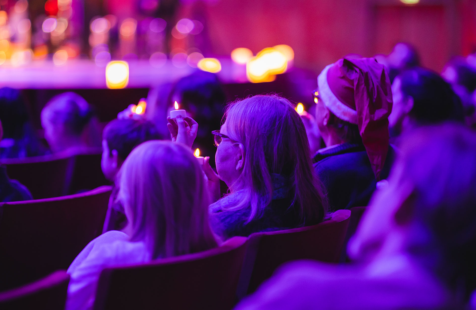 Barn och två vuxna sitter i publiken med stämningsfullt ljus.