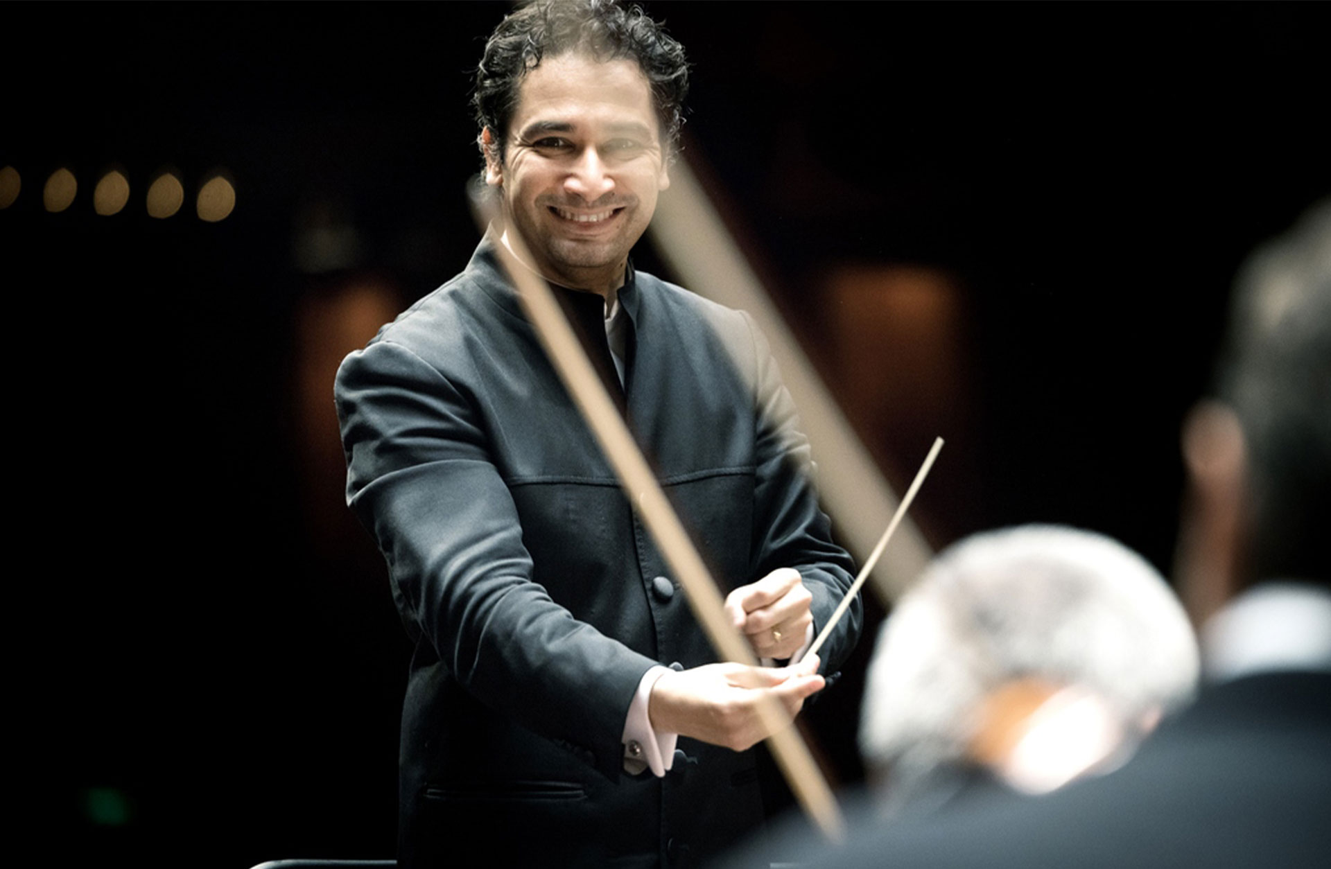 porträtt av Andrés Orozco-Estrada som dirigerar. Han ler, nästan skrattar.