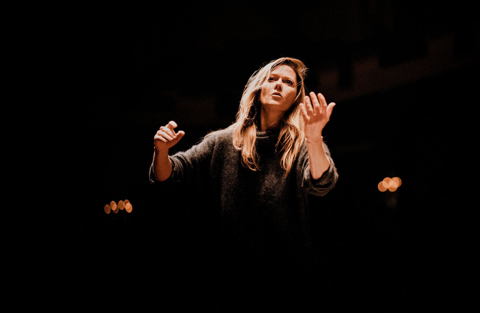 Dirigent Barbara Hannigan står mot svart bakgrund med händerna utsträkta