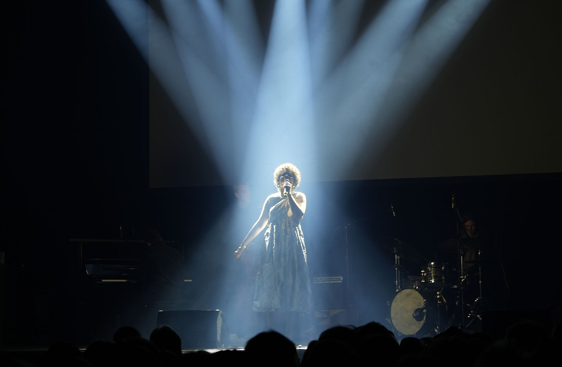 Kvinna står mitt på scen med strålkastarljuset riktat mot sig och håller en mikrofon framför sig.