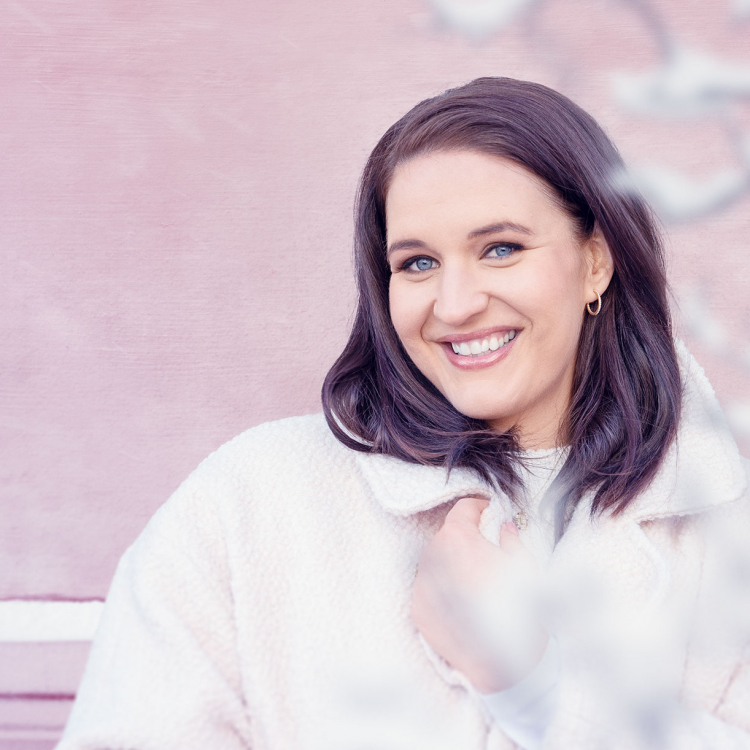 Sångerskan Lise Davidsen i vita vinterkläder mot rosa vägg.