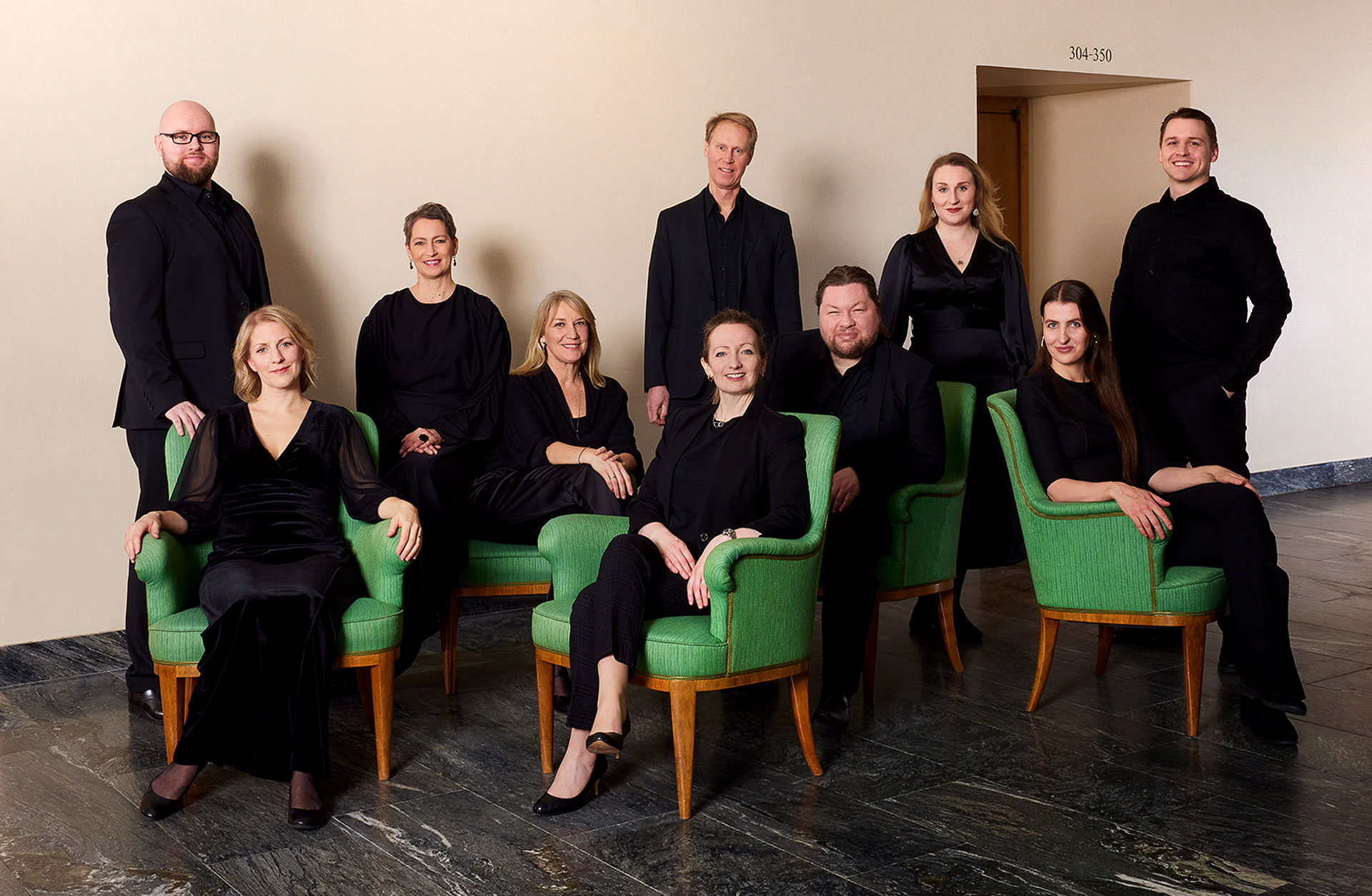 En grupp svartklädda kvinnor och män sitter samlade i en grön soffgrupp.