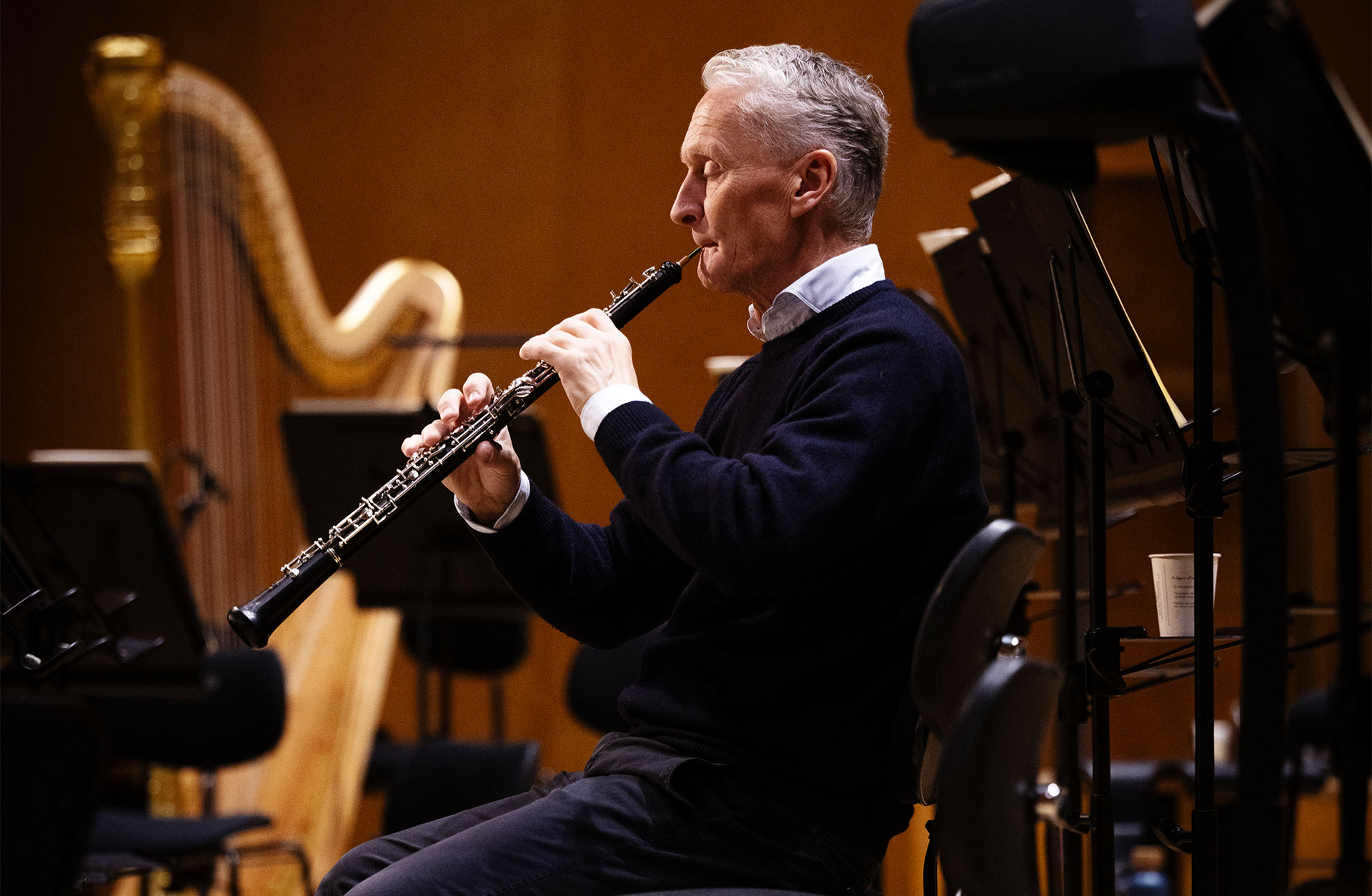Mårten Larsson sitter på en stol på podiet. Han blundar och spelar på sin oboe.