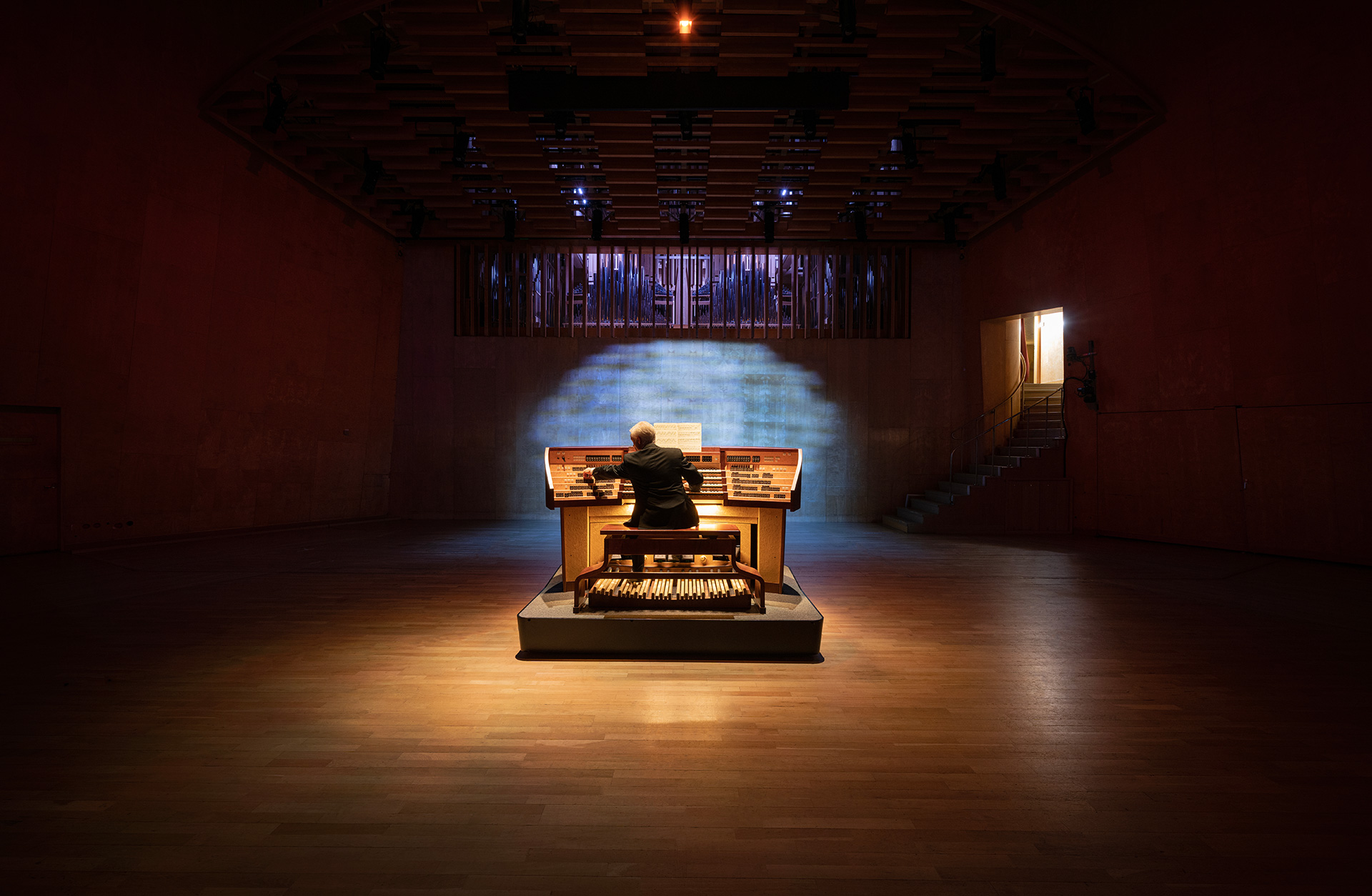 Organist syns bakifrån när han sitter vid instrumentet. Scenen är ljussatt i lila och gult.