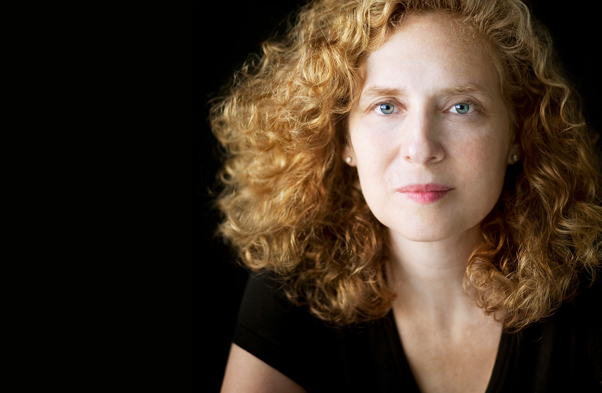 Porträtt av Julia Wolfe. En ung kvinna med rött lockigt hår, som tittar rakt in i kameran med klara blå ögon.