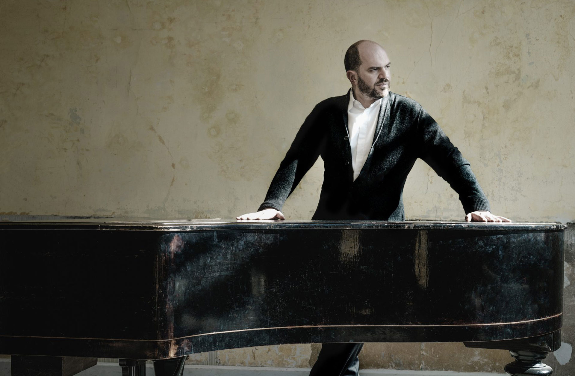 en man står vid sin flygel och blickar åt höger - mot ljuset