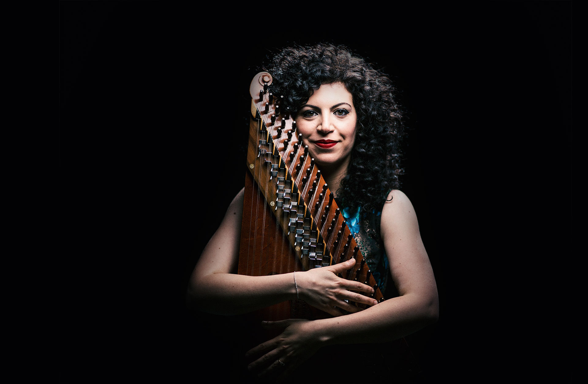 Kvinna står mot mörk bakgrund och omfamnar sitt instrument.