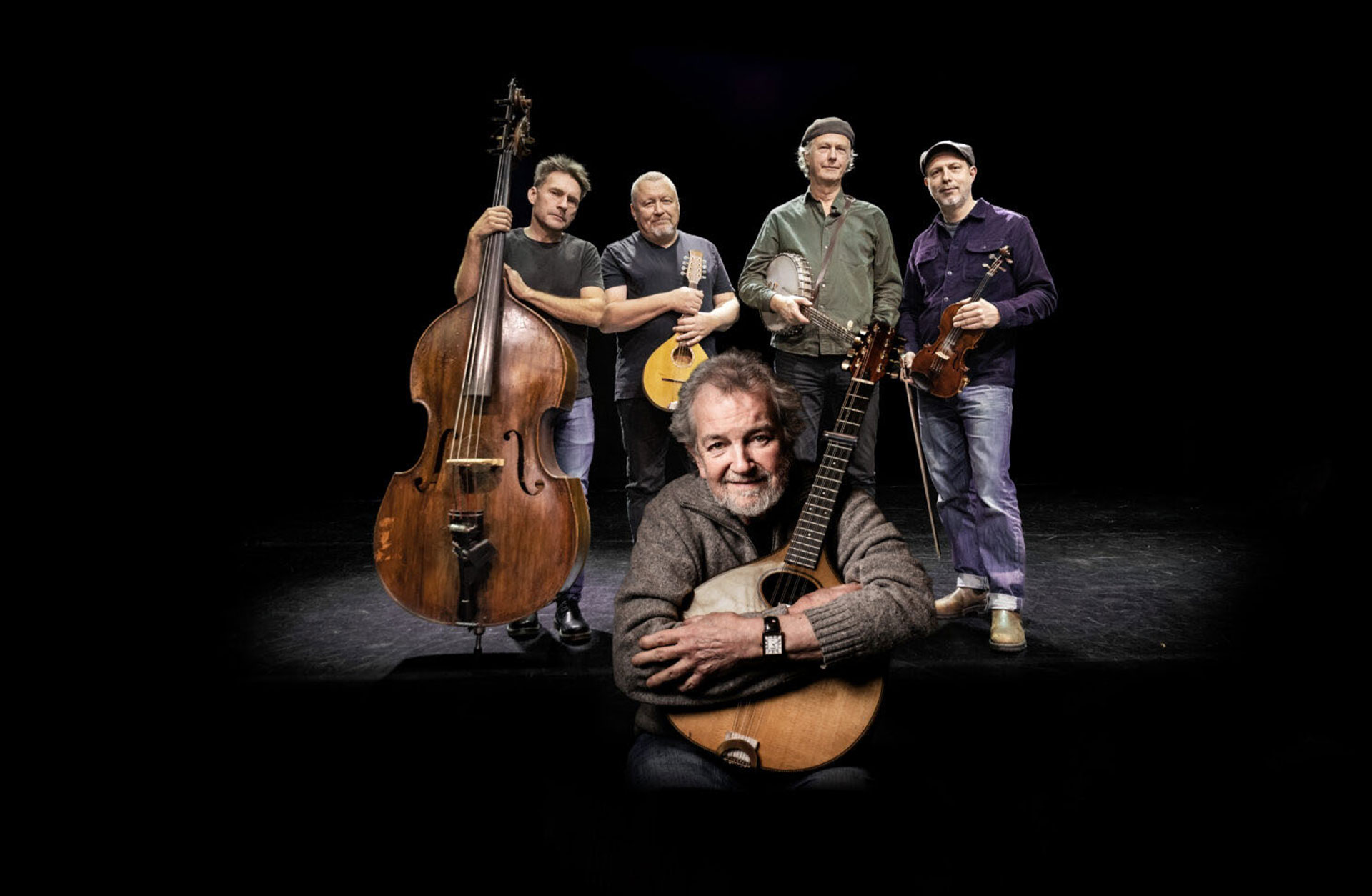 Ensamble står på scen mot svart bakgrund och håller sina instrument