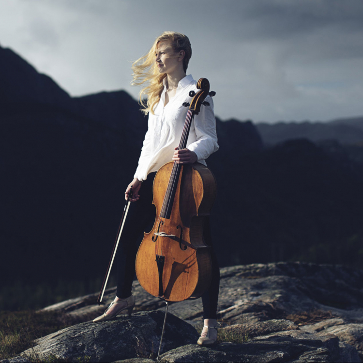Kvinna står på bergstopp med instument i hand med håret fladdrande i vinden