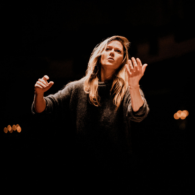 Dirigent Barbara Hannigan står mot svart bakgrund med händerna utsträkta