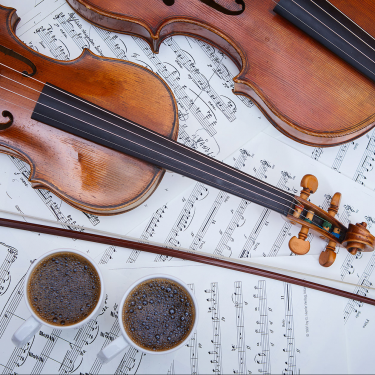 Två fioler ligger på notblad, bredvid står två koppar med kaffe.