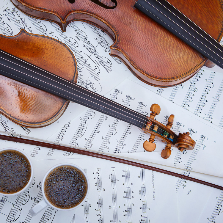 Två fioler ligger på notblad, bredvid står två koppar med kaffe.
