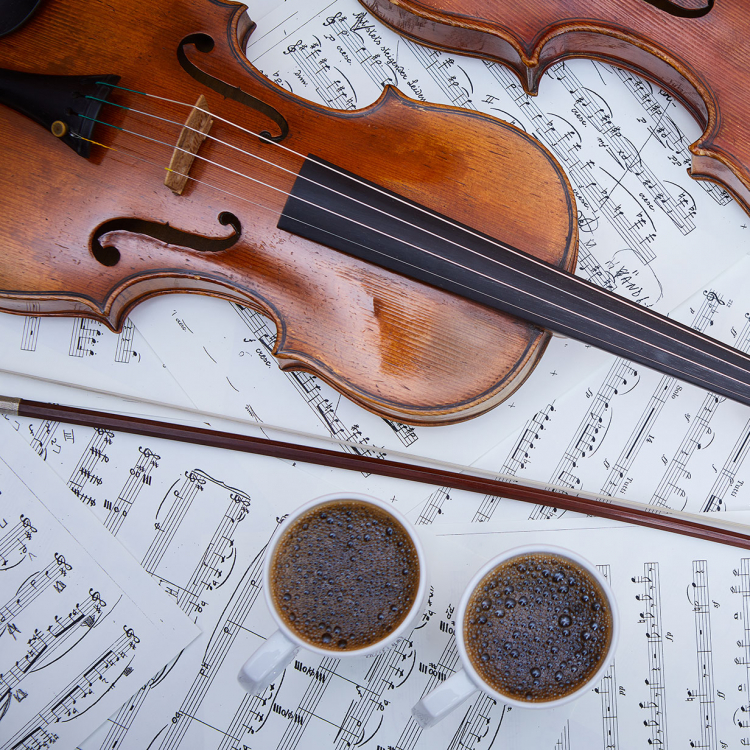 Två fioler ligger på notblad, bredvid står två koppar med kaffe.