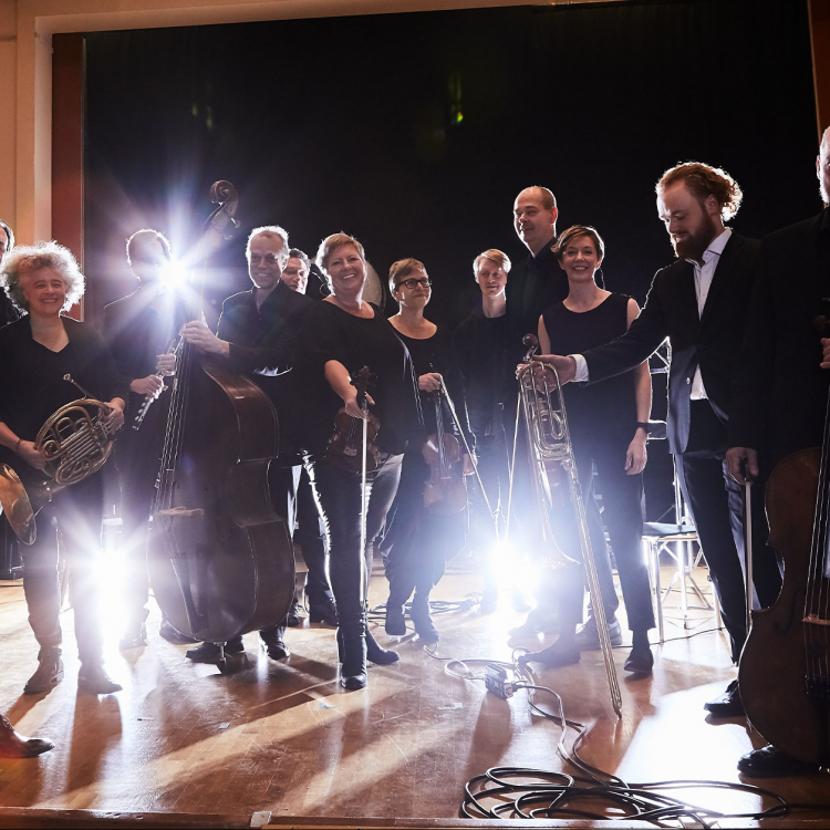 Ensamble står på rad framför kameran och lampor skapar motljuseffekt i bilden.