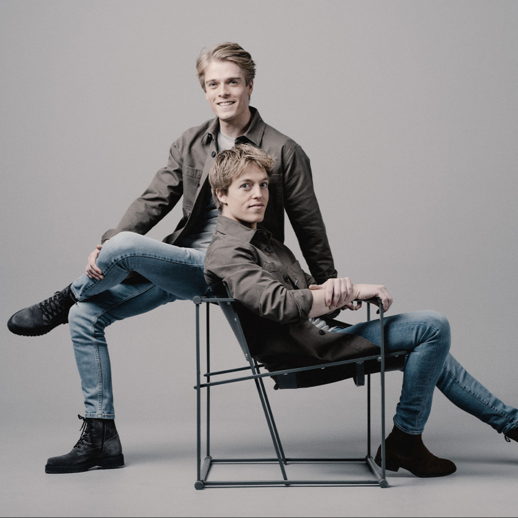Två unga killar, Lucas och Arthur, sitter i olika positioner på var sin stol. De är ledigt klädda.