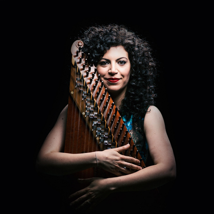 Kvinna står mot mörk bakgrund och omfamnar sitt instrument.