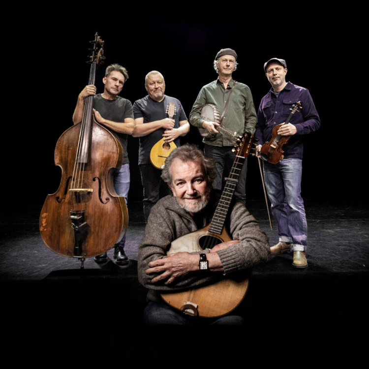 Ensamble står på scen mot svart bakgrund och håller sina instrument