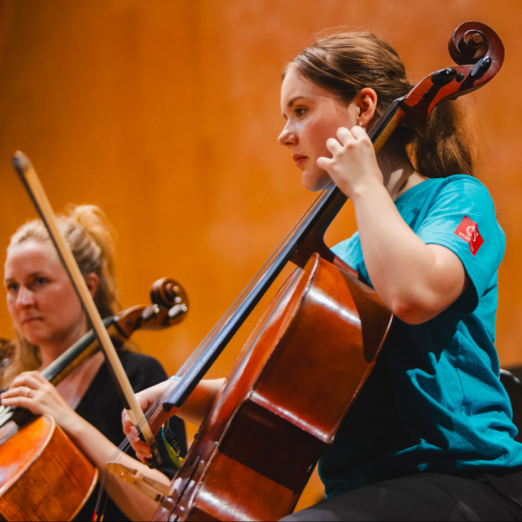 Ung kvinna spelar cello i orkester.