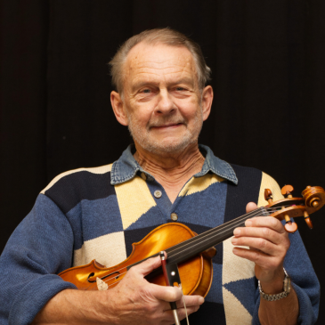 En man med rutig tröja som heter Sven Sjöblom sitter med sin fiol i handen. 