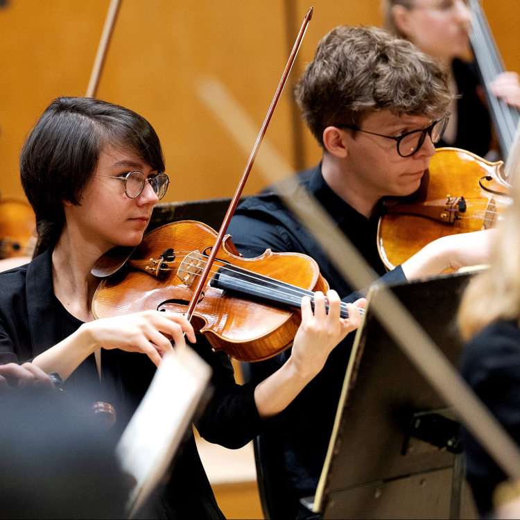 En ung kvinna i mörkt kortklippt hår spelar viola i en orkester.