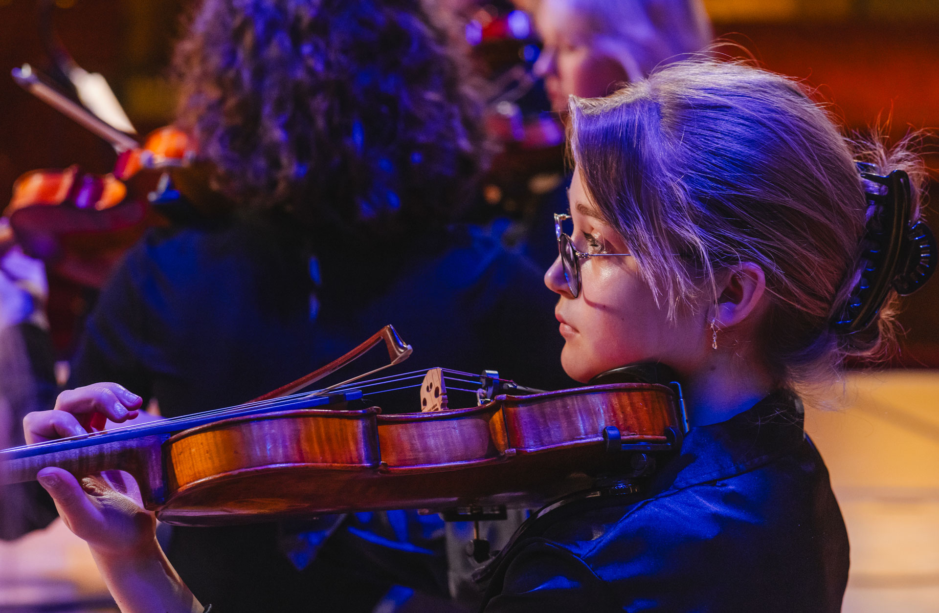 Ung tjej sitter i profil i orkestern och spelar violin.